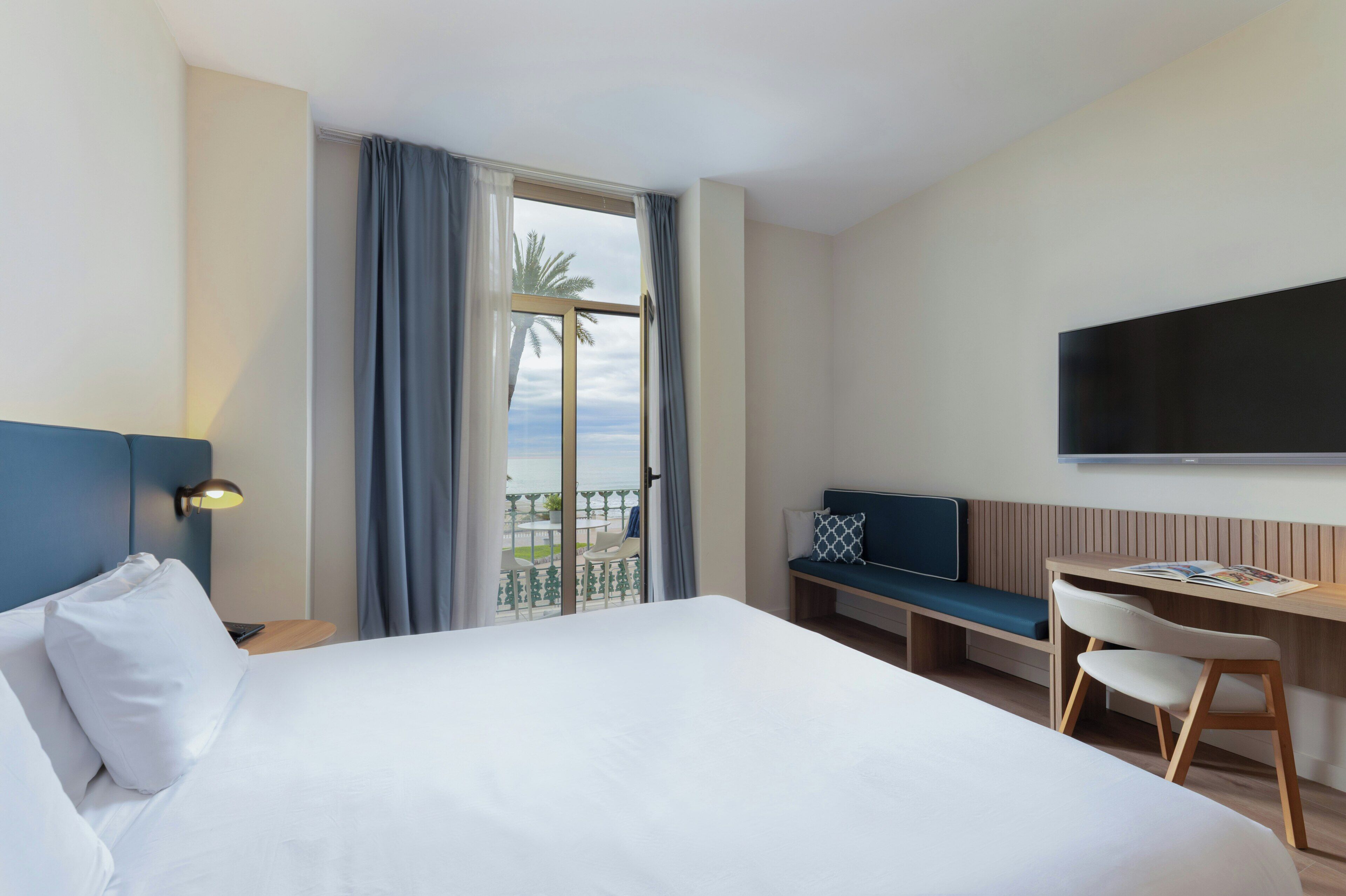 A hotel room with a bed, a desk, a chair, a TV, and a balcony with a view.