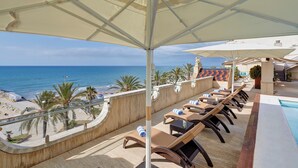 Zona de piscina en la azotea con sillas de descanso y sombrillas con vistas a la playa.