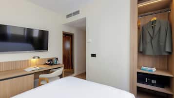 A modern hotel room with a flat-screen TV, wooden desk, white chair, and a walk-in closet with a hanging coat rack.