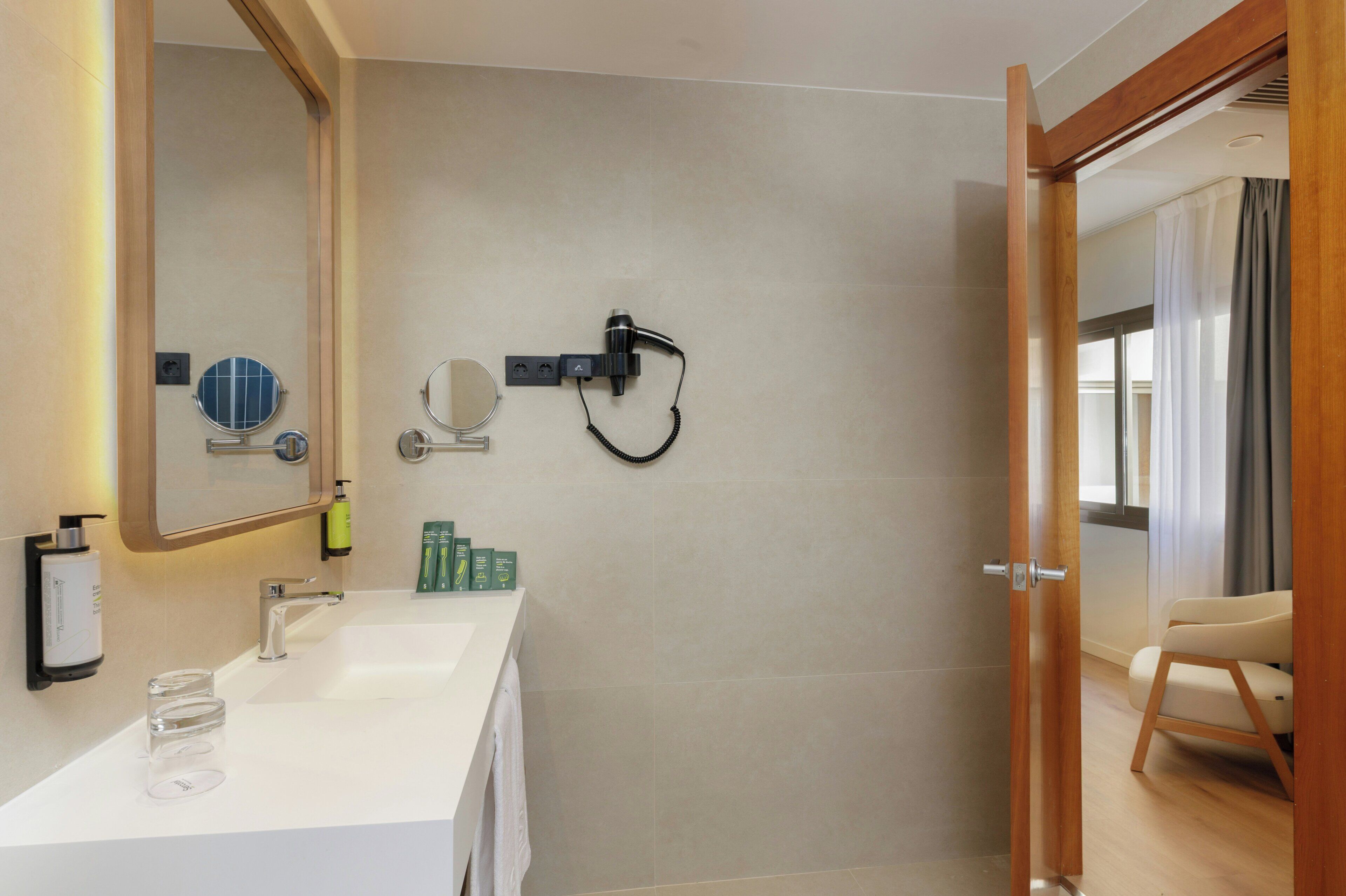 Ein modernes Badezimmer mit einem weißen Waschbecken, einem großen Spiegel und einer an der Wand montierten Duschbrause.