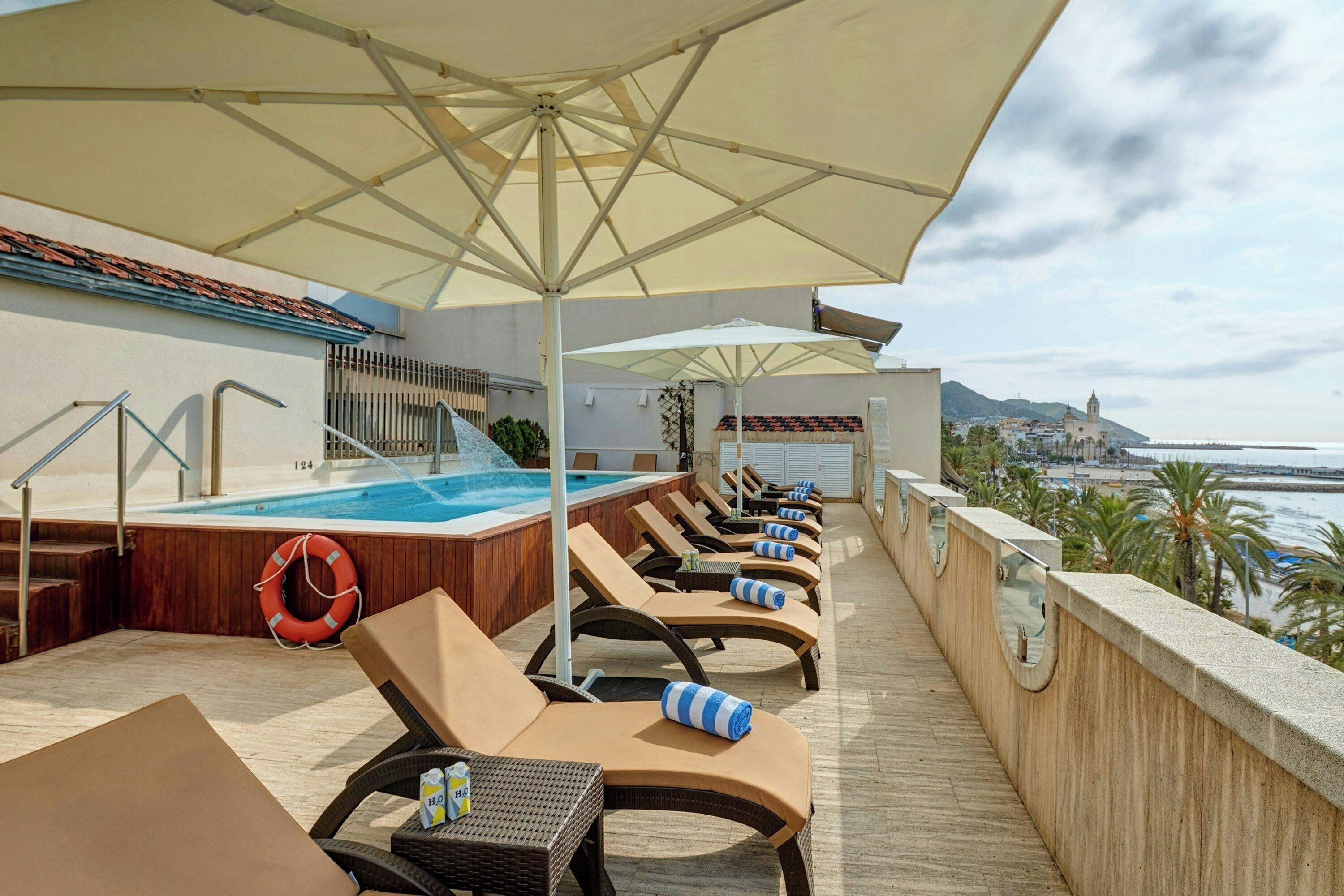 A rooftop pool area with lounge chairs, umbrellas, and a view of the sea.