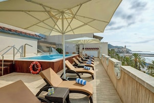A rooftop pool area with lounge chairs, umbrellas, and a view of the sea.