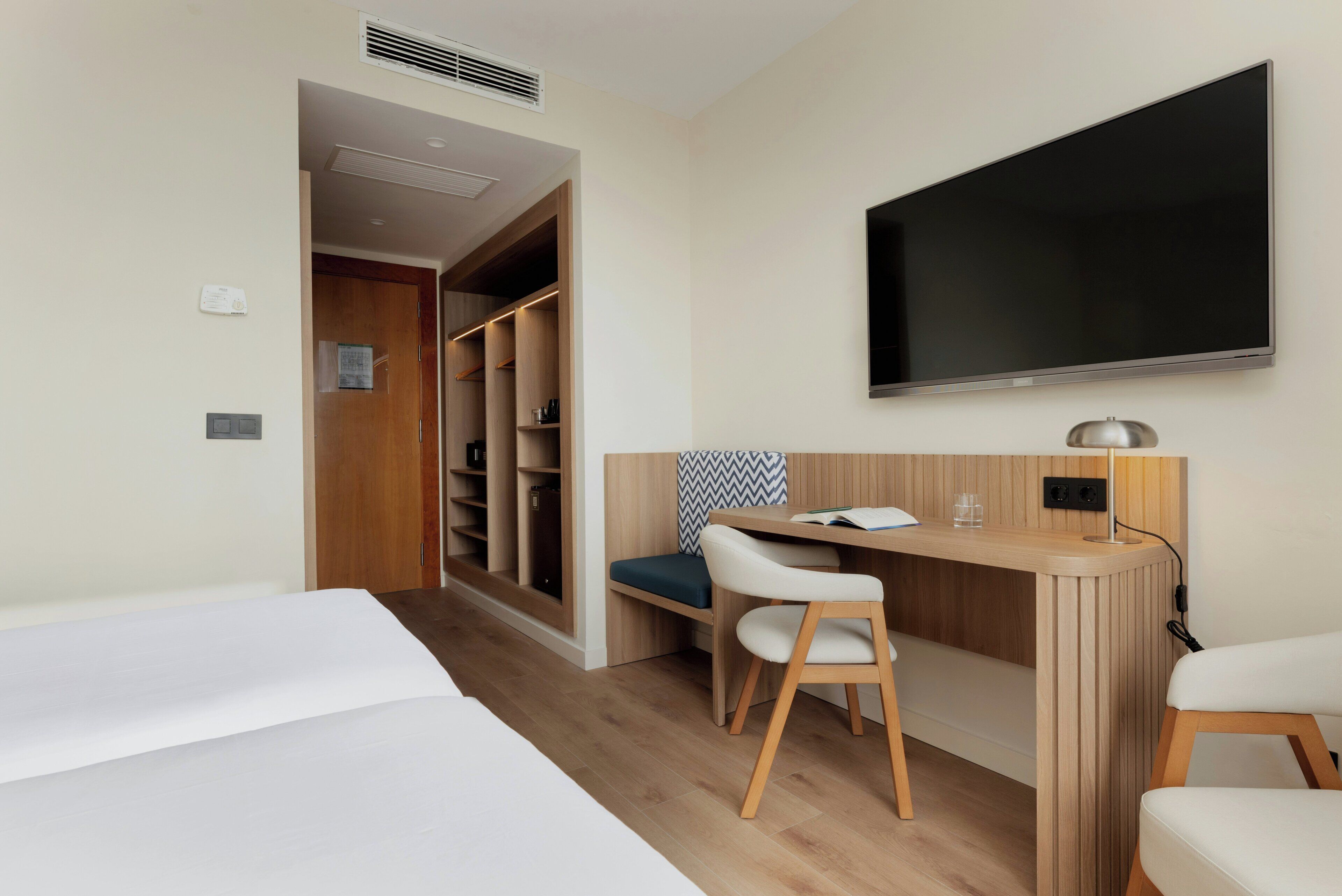 Una habitación de hotel con una cama, un escritorio con una silla, un televisor y un armario.