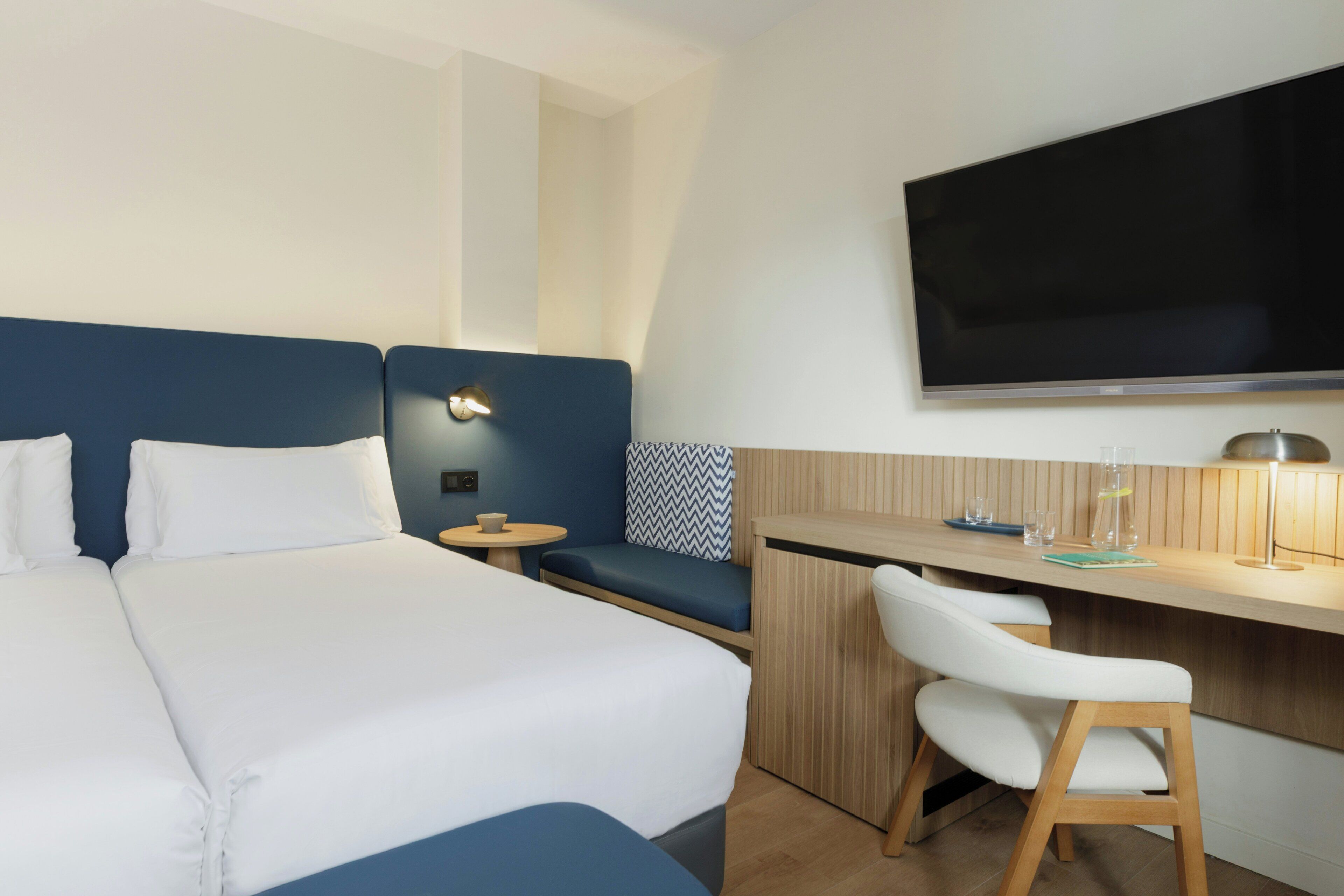 Une chambre d’hôtel avec un grand lit, un bureau avec une chaise, une télévision et une petite table avec une tasse et un verre.
