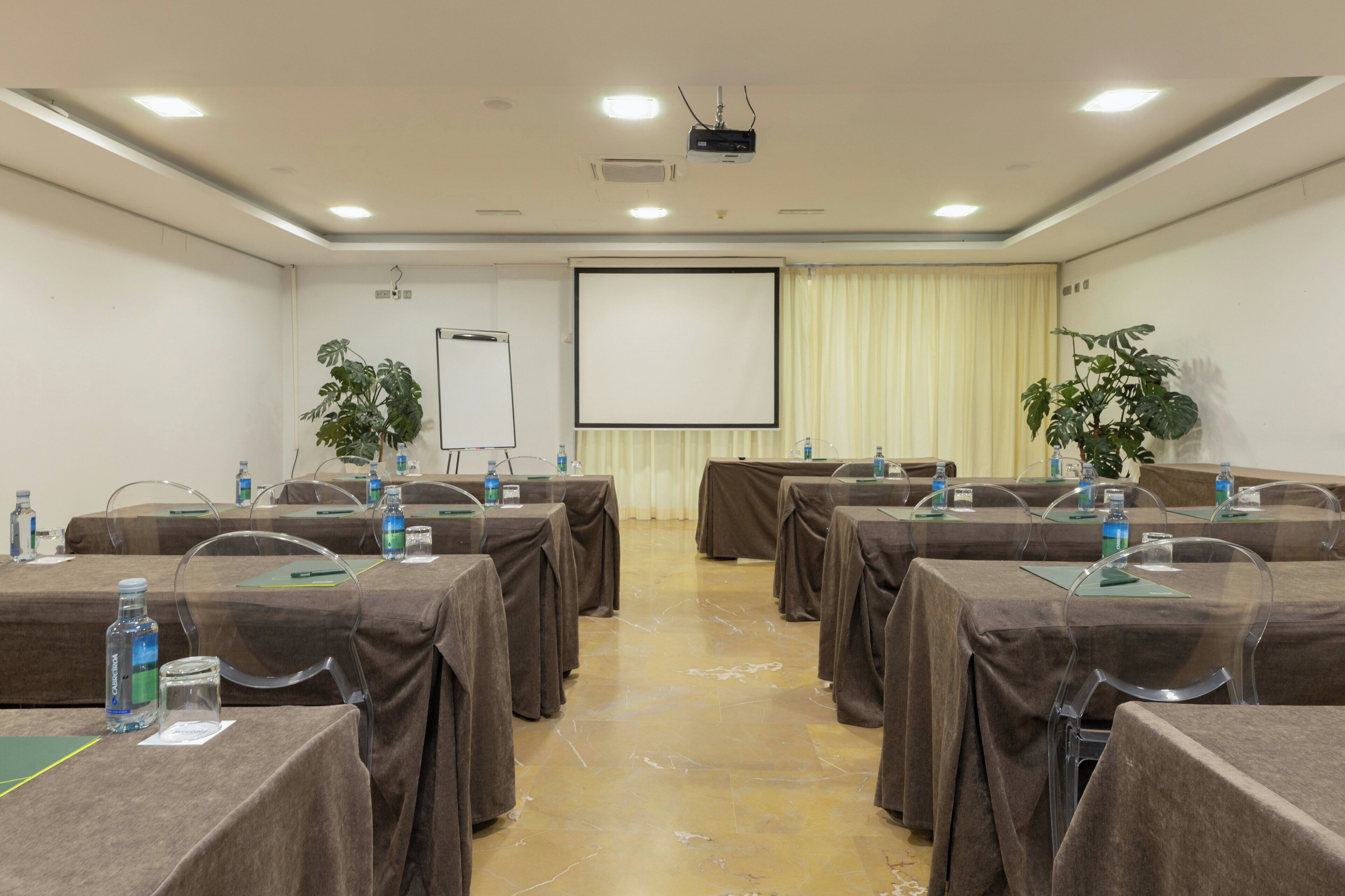 A conference room with tables, chairs, a projector, and a screen.
