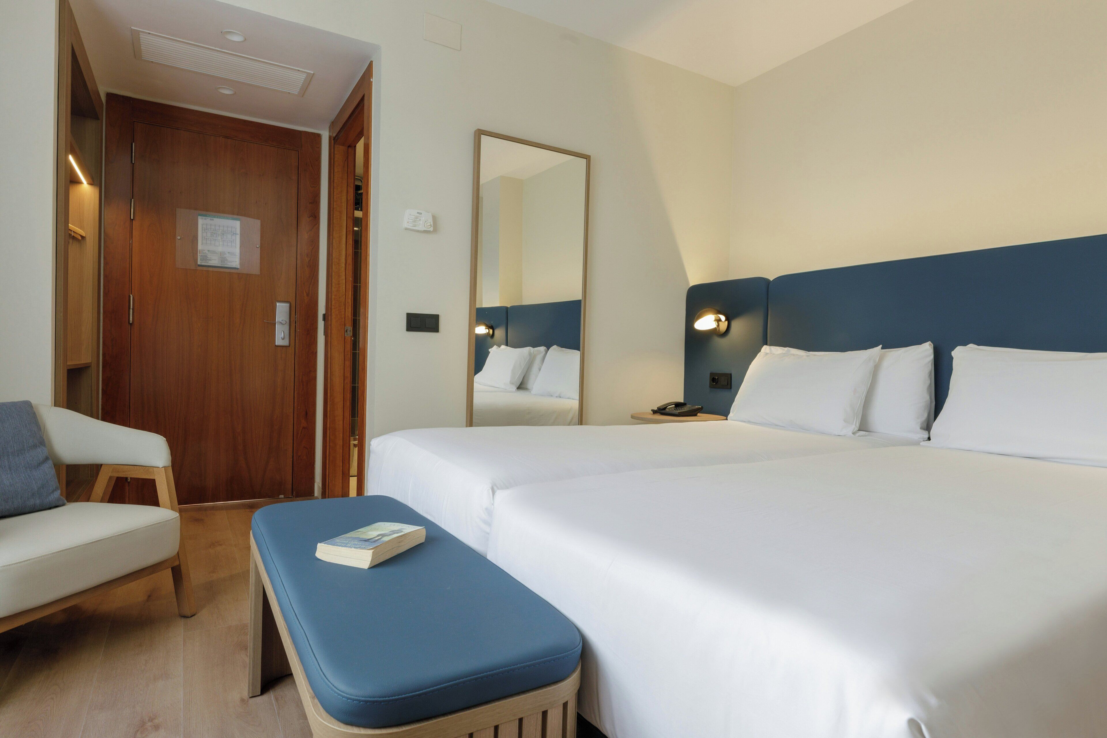 Ett hotellrum med två sängar, en trädörr, en spegel, ett sängbord och en stol.