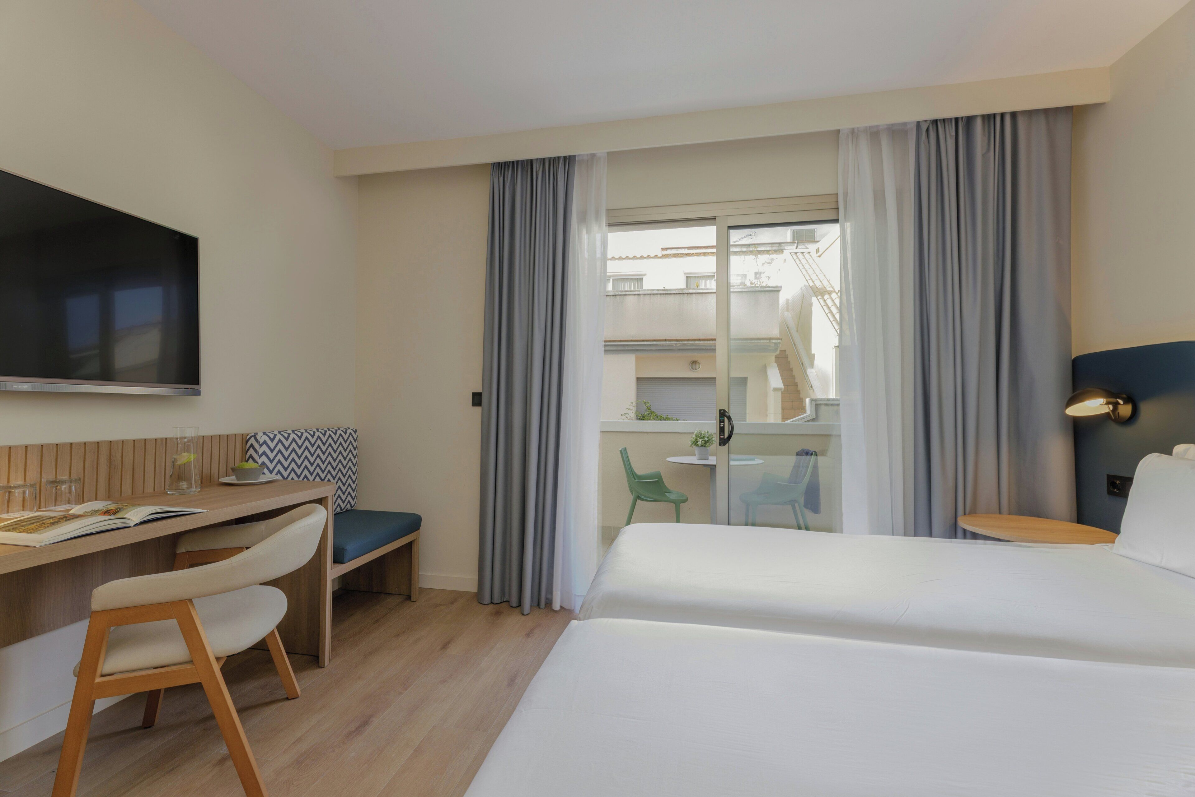 Una habitación de hotel con cama, escritorio con silla, televisión y balcón con mesa y sillas.