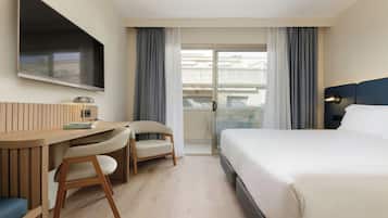 Una camera d'albergo con un letto, una scrivania con una sedia, una TV a parete e un balcone con tende.