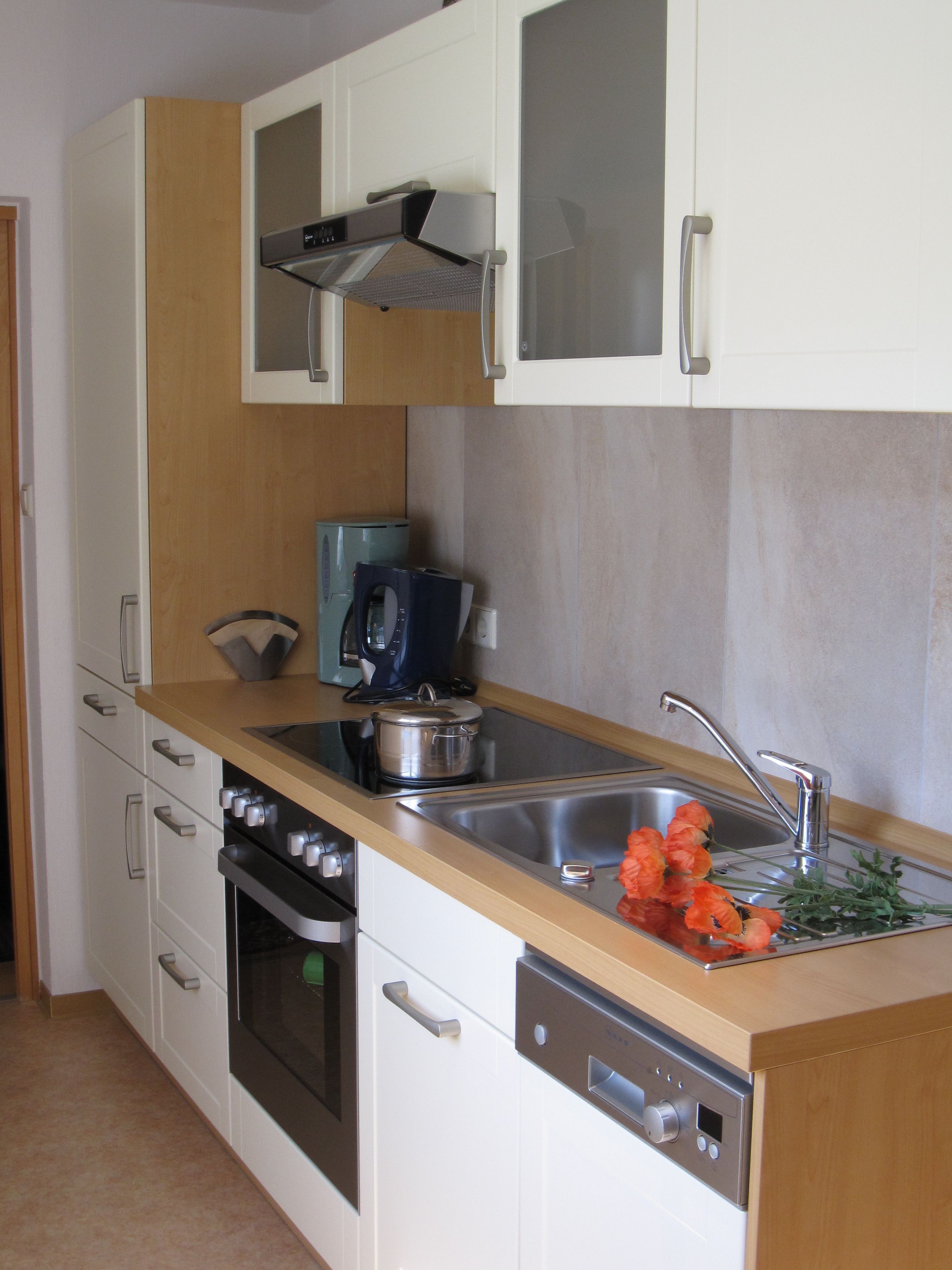 A modern kitchen with white cabinets, a stainless steel sink, and a built-in oven.