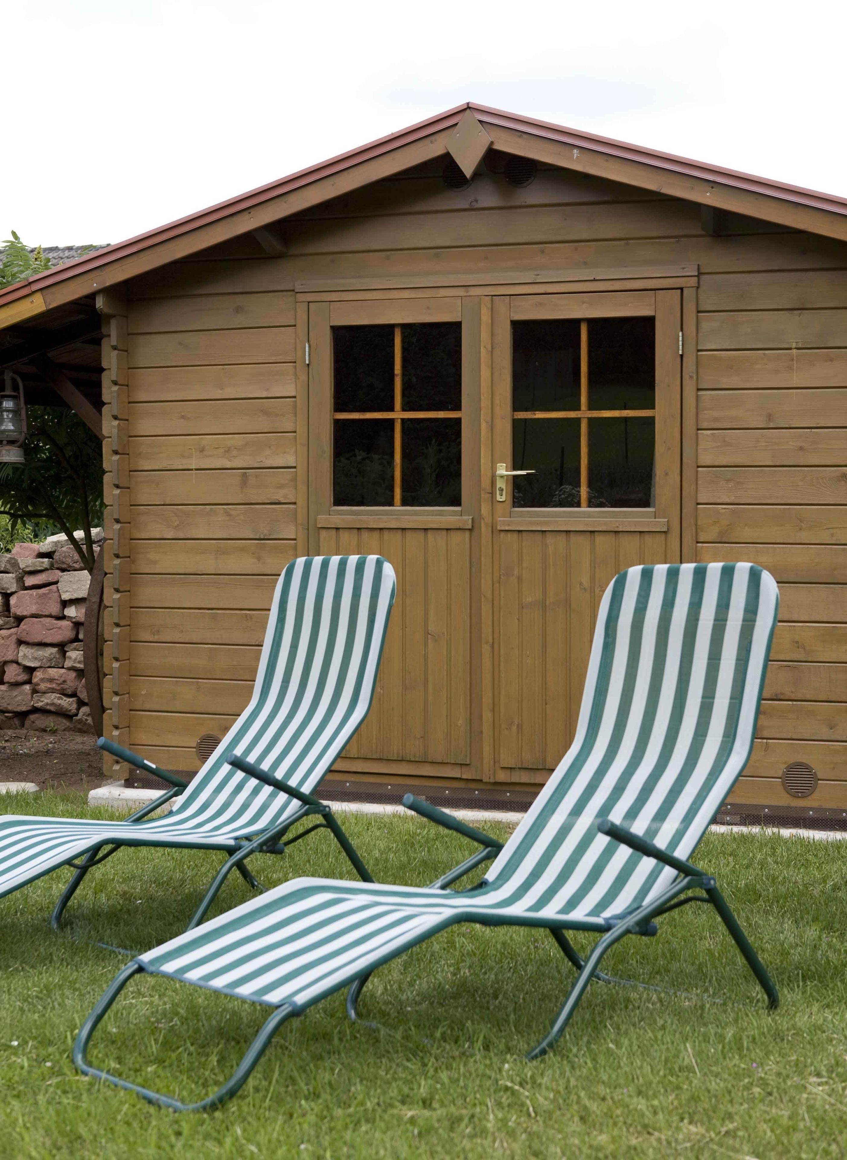 Two striped lounge chairs in front of a wooden building with a gabled roof and a double door.