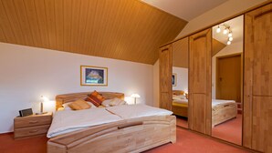 Een slaapkamer met een houten bed, een nachtkastje, een bedlampje en een grote spiegelkast.
