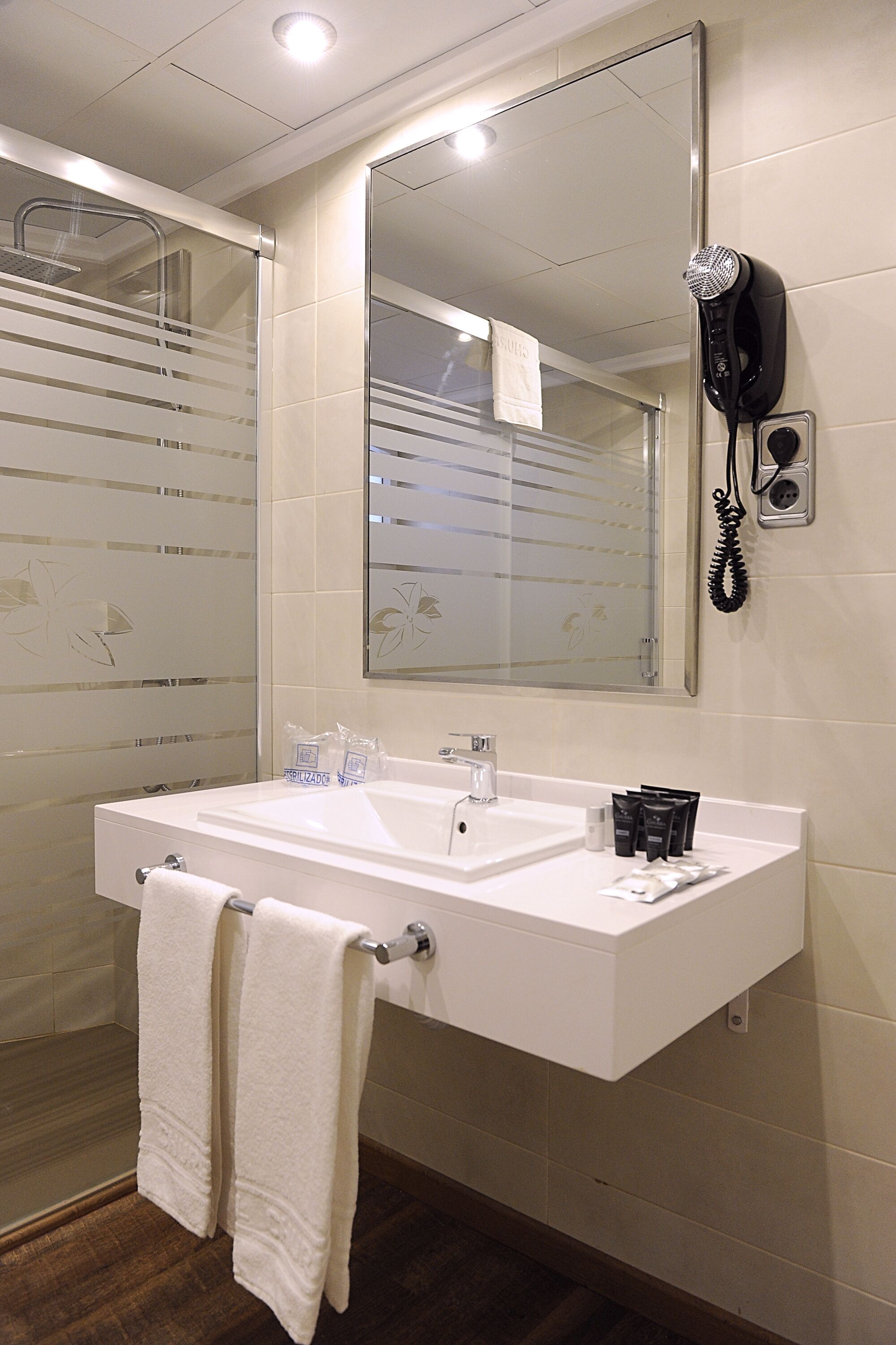 Un baño con un espejo grande, dos lavamanos, un secador de pelo y un perchero para toallas.