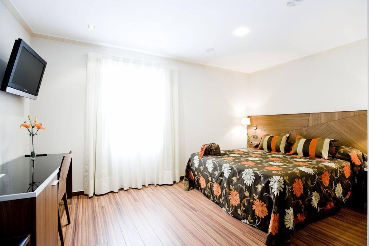 A hotel room with a bed, a desk, a TV, and a window with curtains.