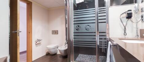 A modern bathroom with a glass shower enclosure, a toilet, bidet, and a sink with a towel hanging on the wall.