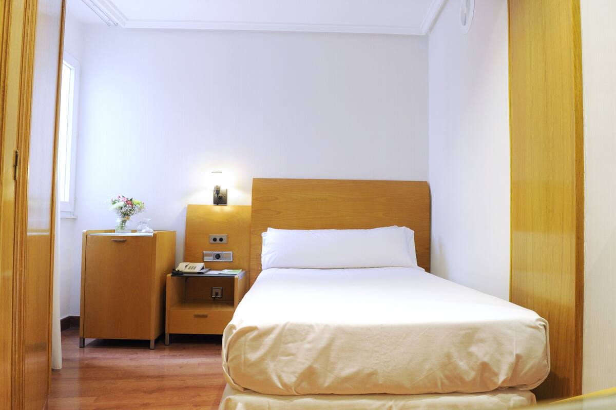 A hotel room with a bed, a nightstand, a lamp, and a small table with a vase.