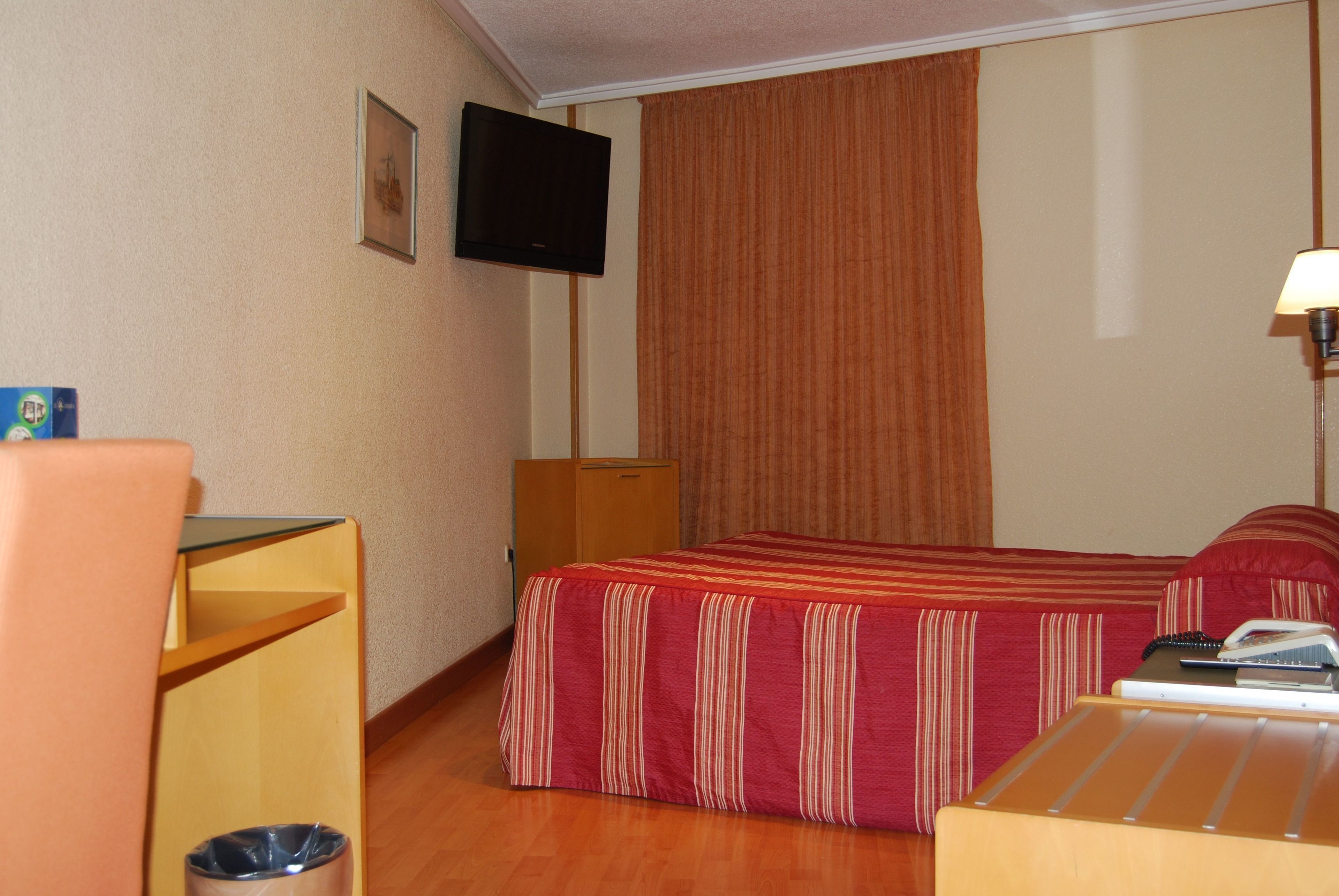 A hotel room with a bed, a desk, a chair, a TV, and a lamp.