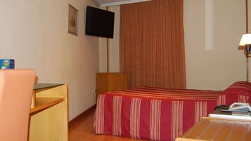 A hotel room with a bed, a desk, a chair, a TV, and a lamp.