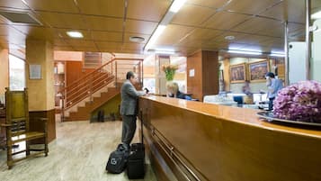 Zona de recepción con un mostrador de madera, una escalera y vistas al vestíbulo.