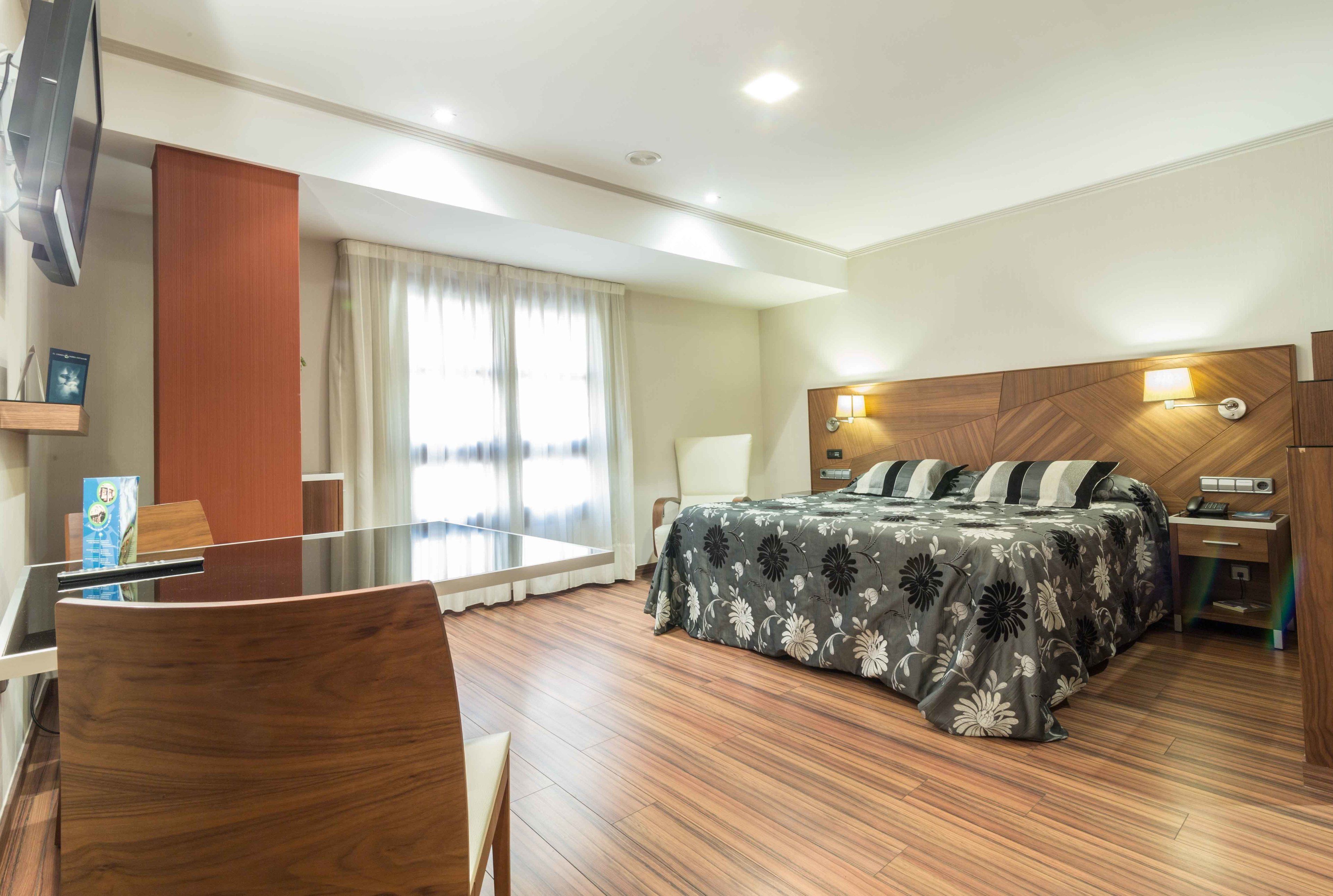 Une chambre d’hôtel équipée d’un lit, d’un bureau, d’une chaise, d’une télévision et d’une fenêtre avec des rideaux.
