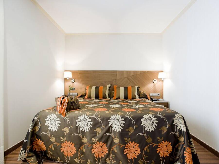 Una habitación de hotel con cama, almohadas, una mesita de noche y una lámpara.