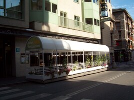 Un restaurante con un área de estar exterior cubierta, entrada visible y un letrero que indica que es un restaurante.