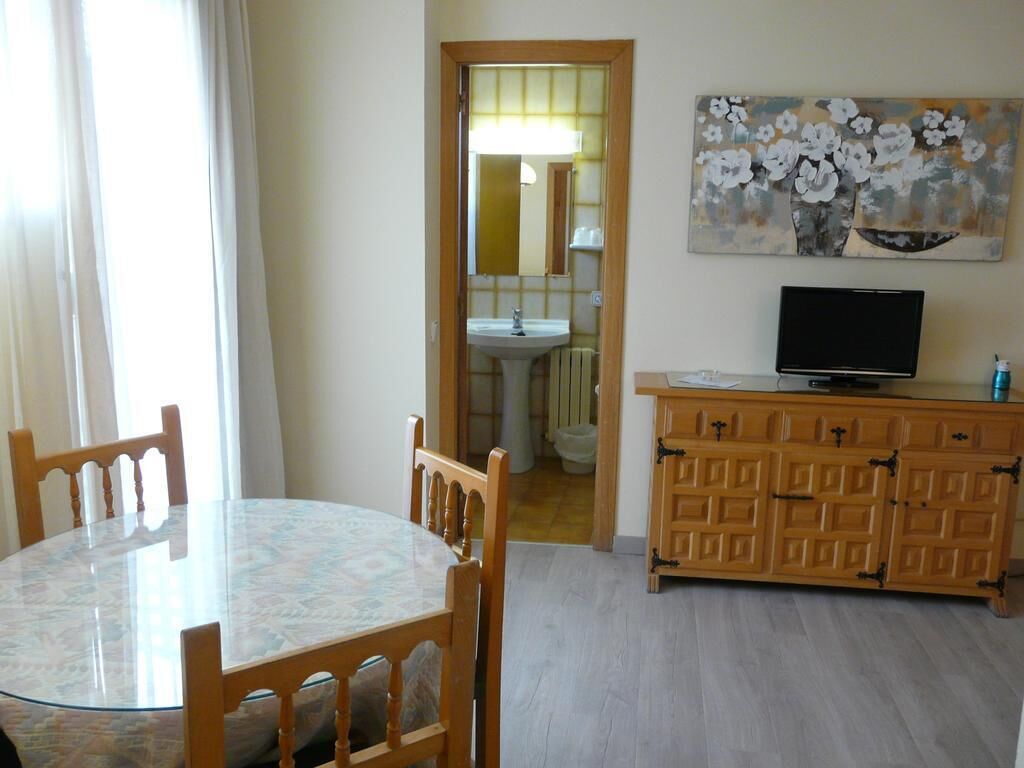 A dining area with a round table and chairs, a wooden cabinet with drawers, a television, and a painting on the wall.