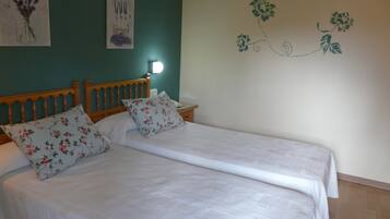 A double bed with floral bedding and two pillows, a wooden headboard, a bedside table with a lamp, and a wall with a floral decal.