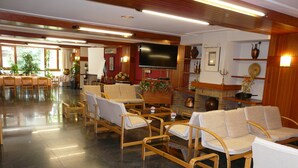 A spacious lobby with a long reception desk, multiple seating areas with cushioned chairs, a flat-screen TV mounted on the wall, and a fireplace with decorative items. - Nice (La Seu d'Urgell)