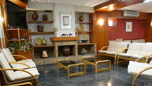 A lobby with wicker chairs, a fireplace, and shelves with decorative items. - Nice (La Seu d'Urgell)