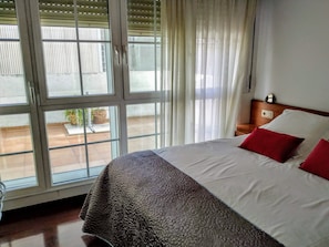 A hotel room with a large bed, a nightstand, and a view through a window with blinds.