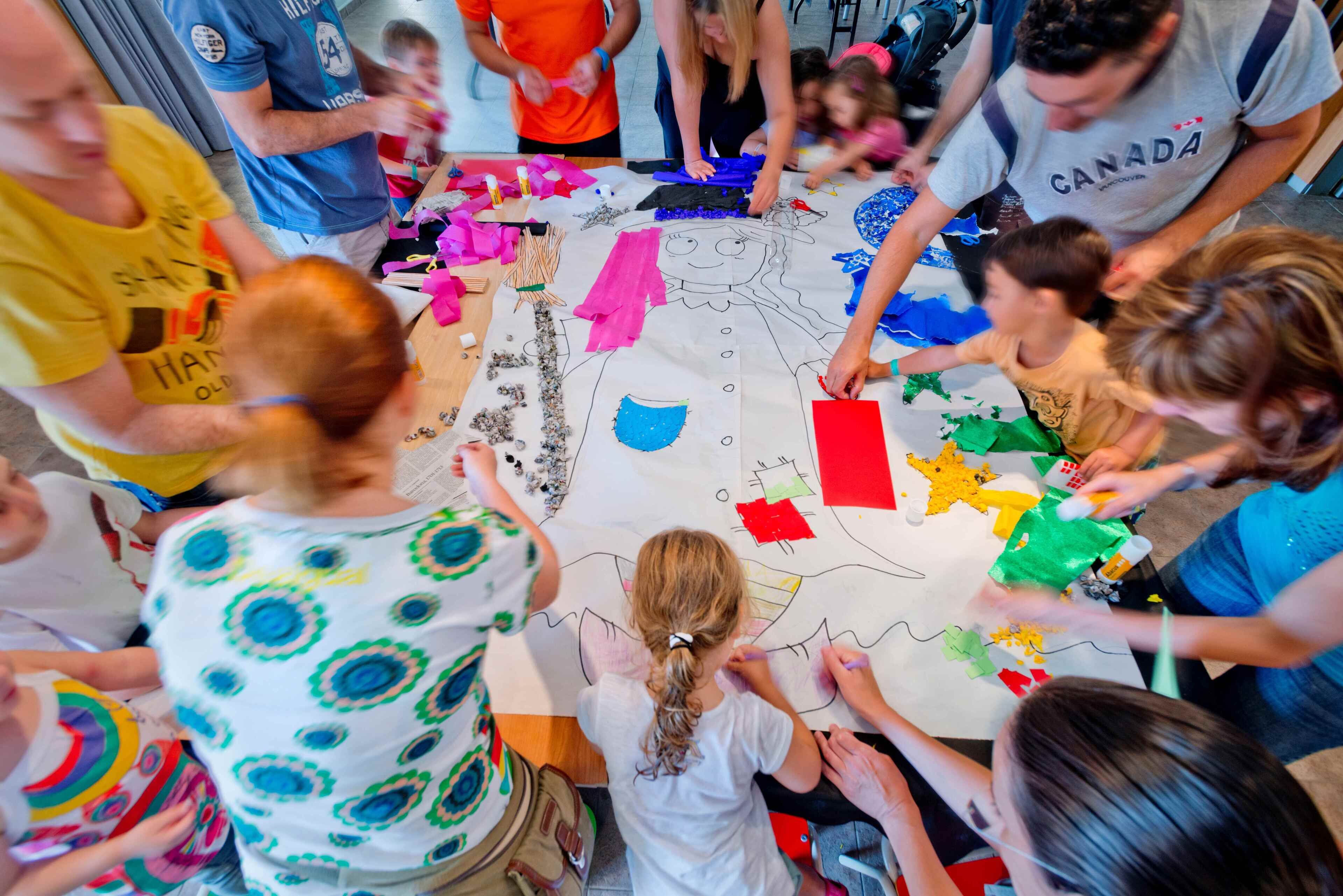 A group of people engaged in a collaborative art project, with various colored papers and materials spread out on a table.