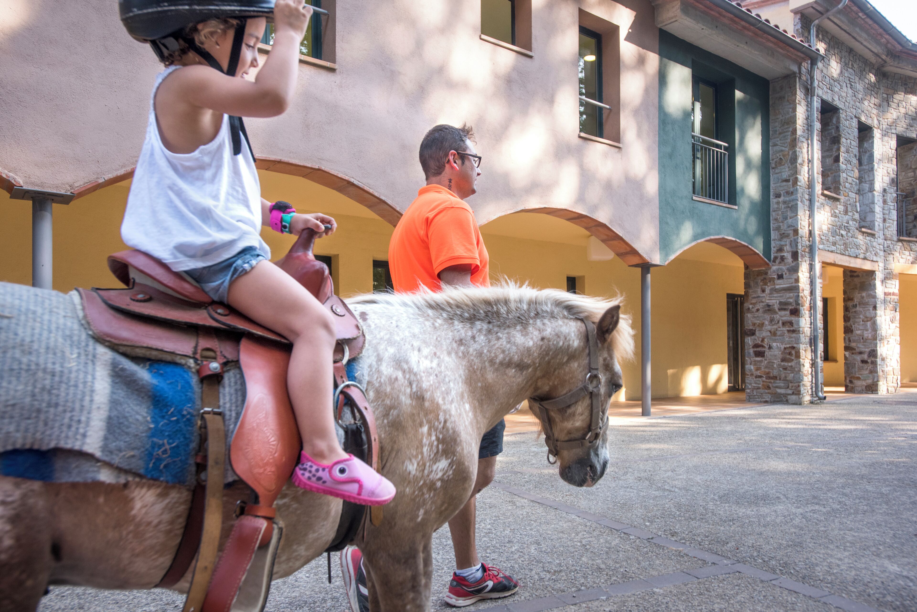 A person riding a horse in an outdoor area with stone buildings in the background.