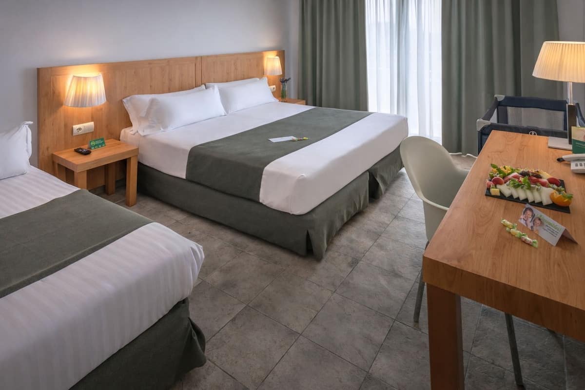 Habitación de hotel con dos camas, un escritorio y una bandeja de frutas, y vista a la calle.