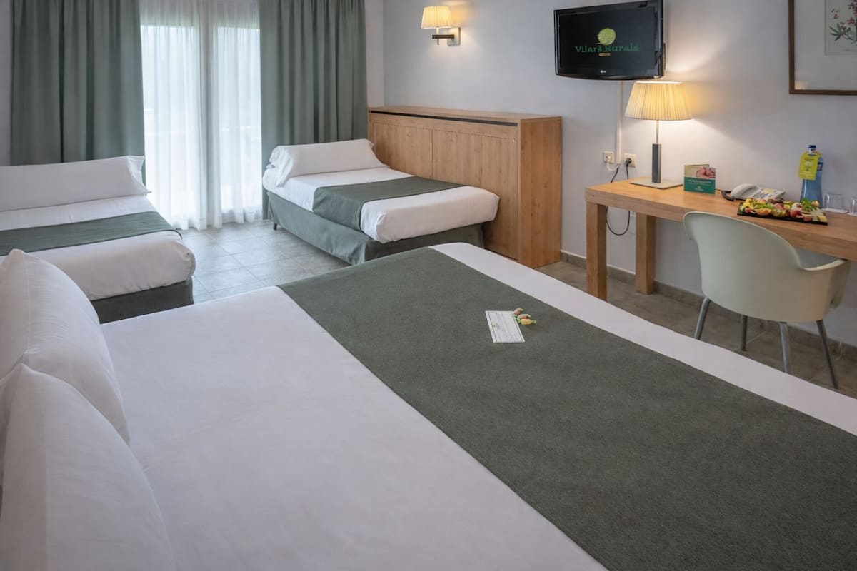 Habitación de hotel con dos camas, un escritorio con silla, televisor y ventana con cortinas.