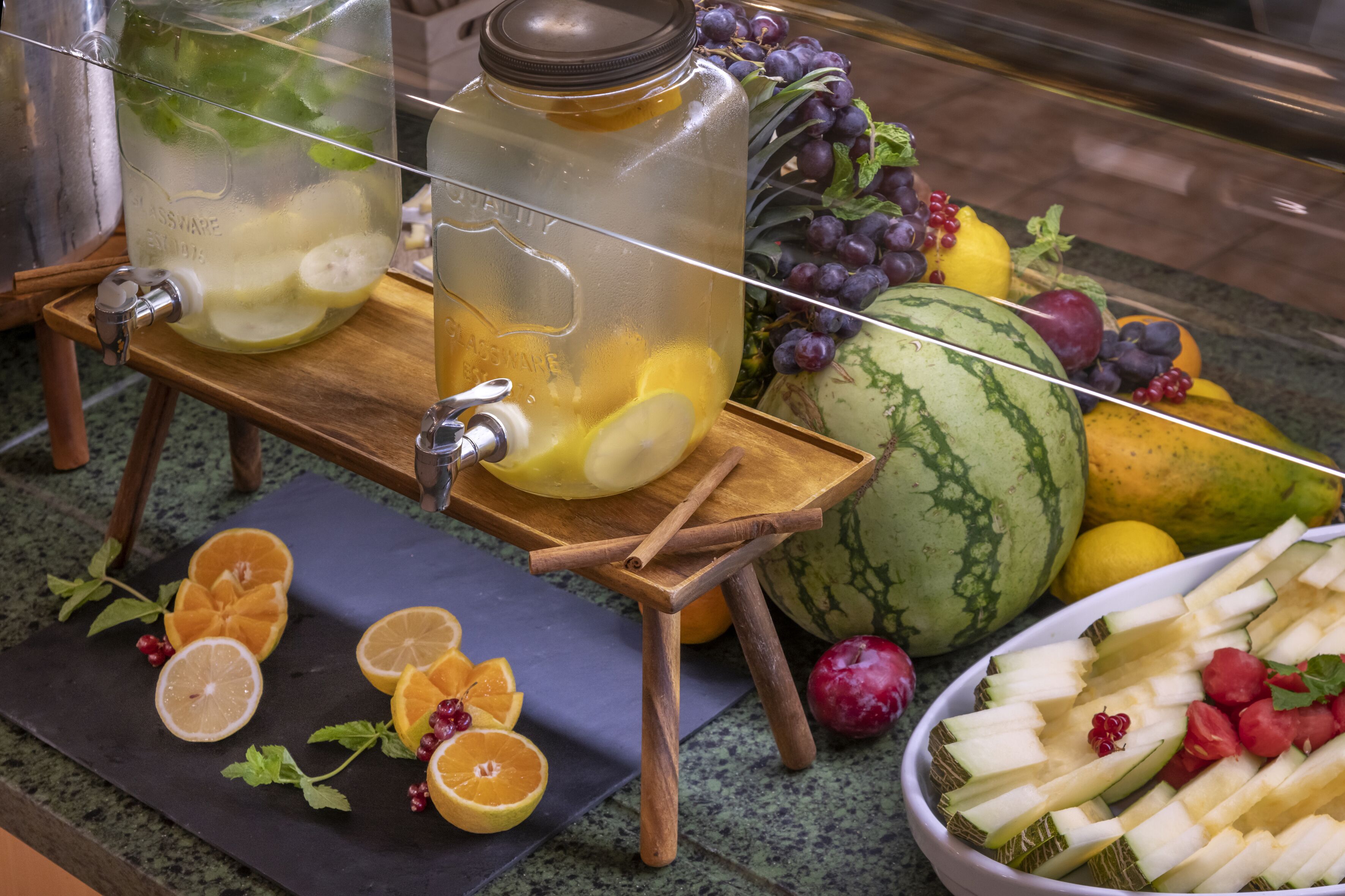 Un espace dédié aux boissons, équipé de deux grands distributeurs, d’une variété de fruits frais et d’un saladier rempli de légumes coupés.