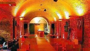 Een lange, smalle gang met een gewelfd plafond, aan weerszijden voorzien van tafels en stoelen.
