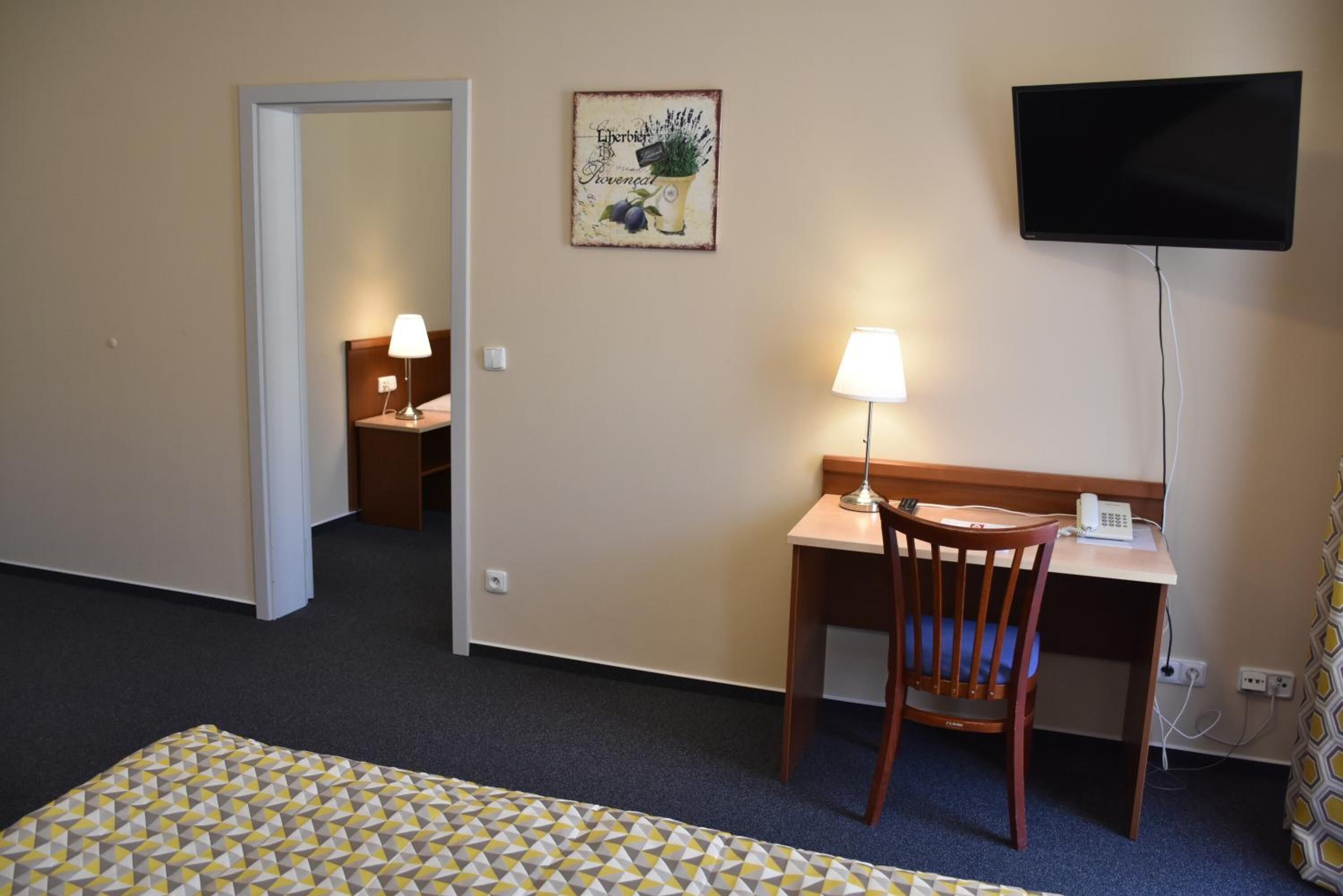 Et hotelværelse med en seng, et skrivebord med stol, et fjernsyn og et lille bord med lampe.