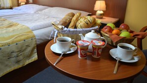 Een hotelkamer met een netjes opgemaakt bed, een ontbijttafel met croissants, fruit, koffie en yoghurt.