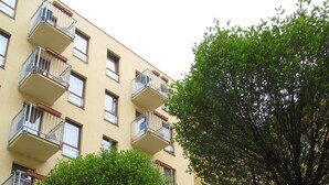 Een meerlaags gebouw met balkons, een boom op de voorgrond en een heldere lucht.
