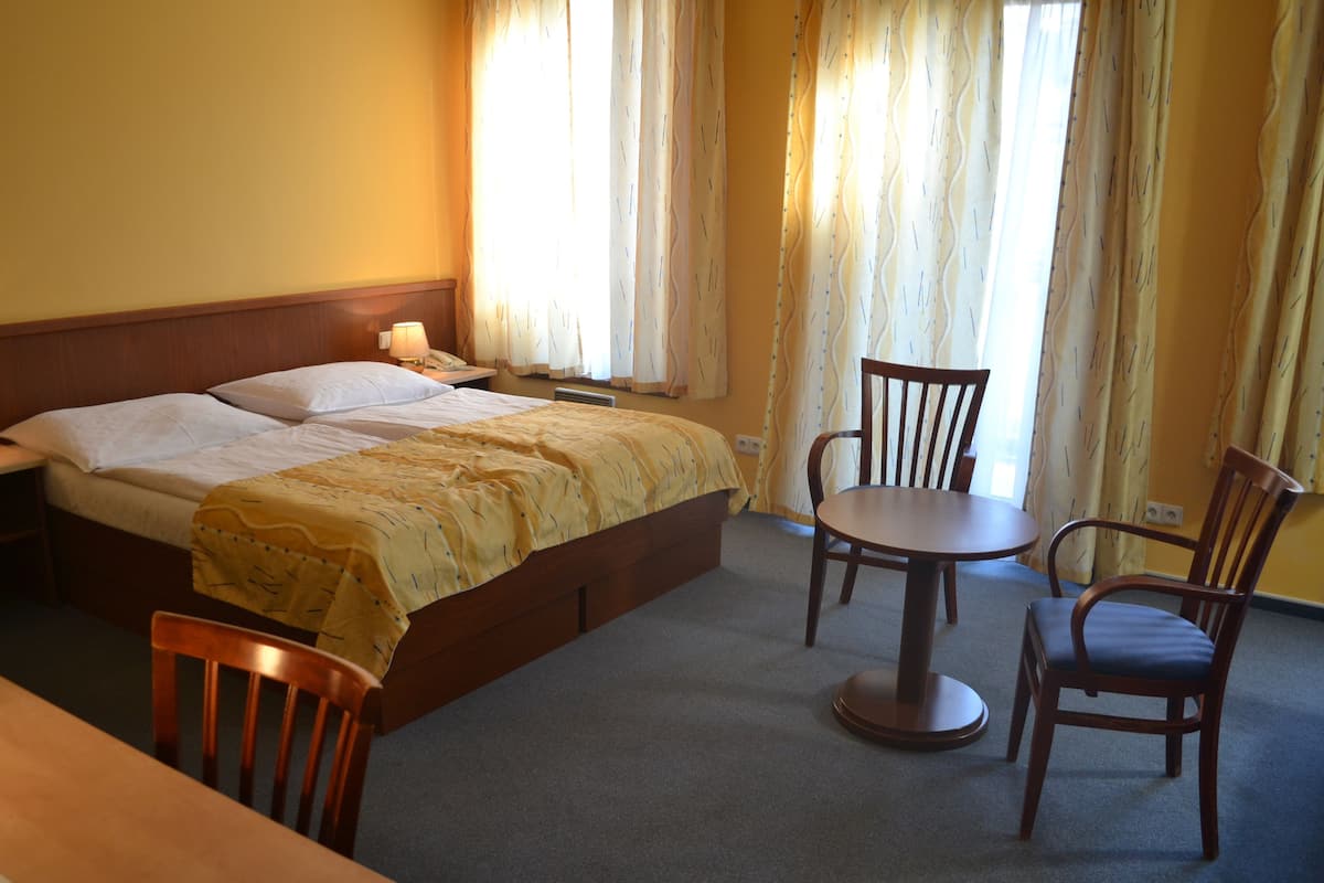 A hotel room with a bed, two chairs, a small table, and a nightstand.