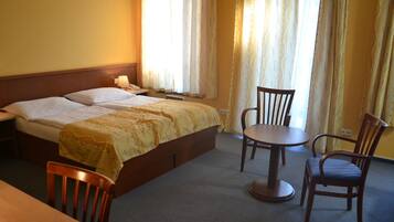 A hotel room with a bed, two chairs, a small table, and a nightstand.