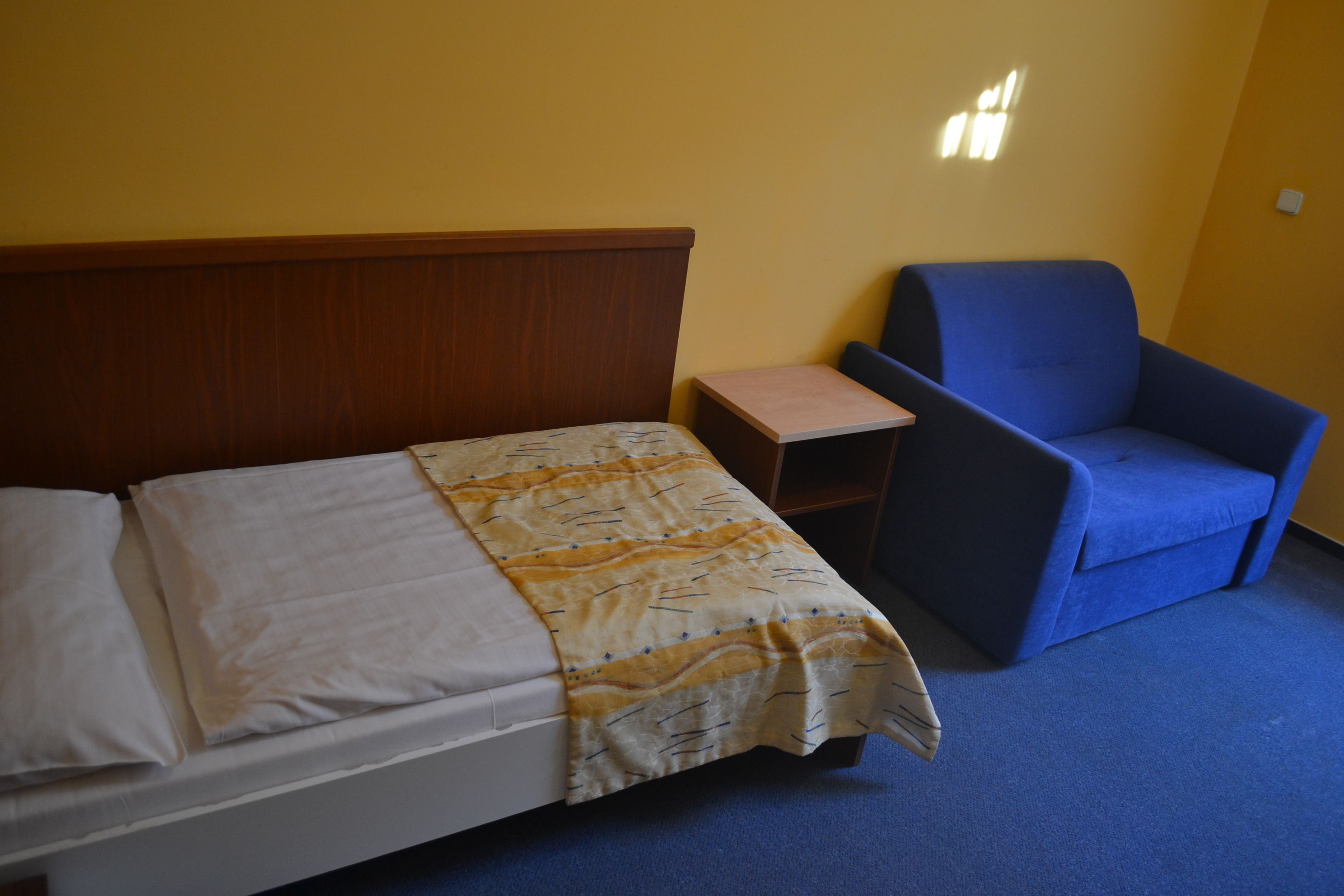 Ein Hotelzimmer mit einem Bett, einem kleinen Tisch, einem blauen Sessel und einer Wandleuchte.