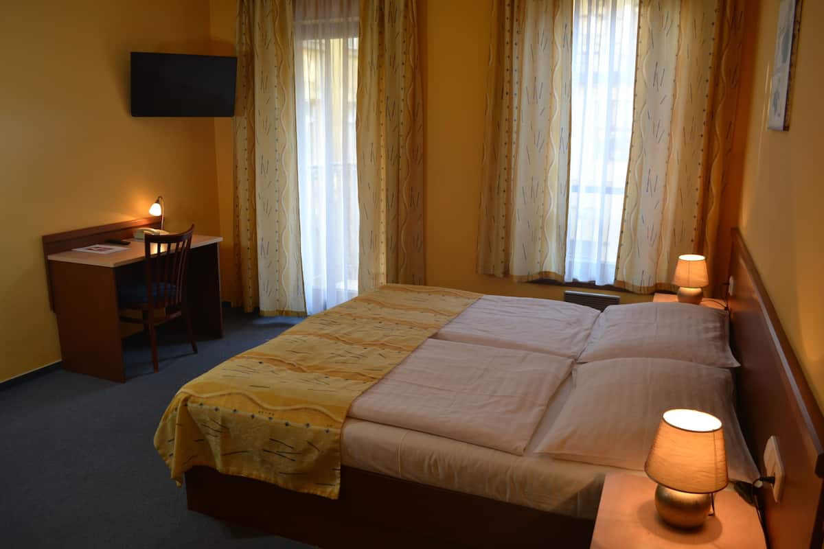 A hotel room with a bed, a desk, a chair, and a TV on the wall.