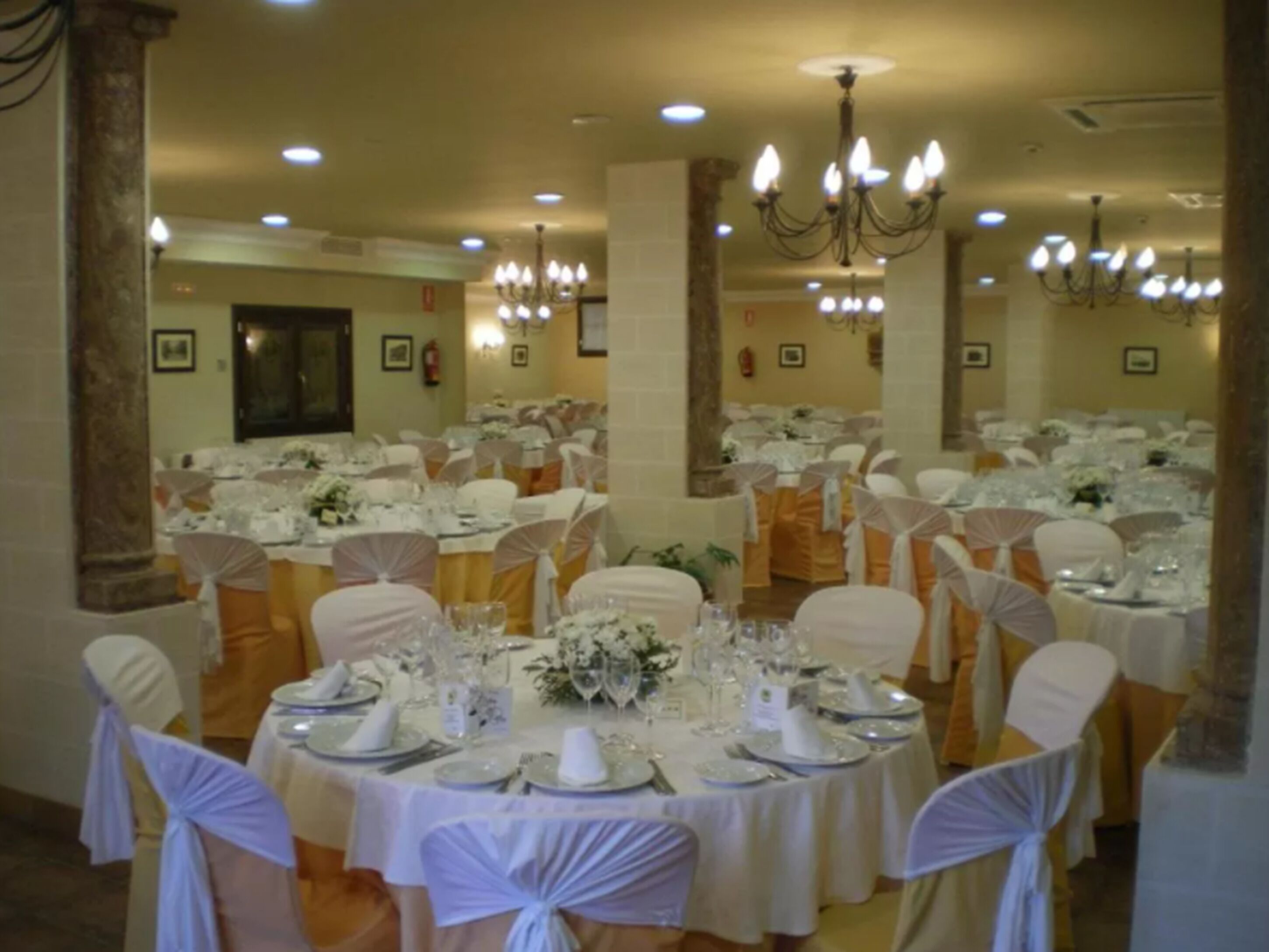 Uma sala de banquetes com mesas redondas preparadas para um evento formal, com toalhas brancas, talheres e copos.