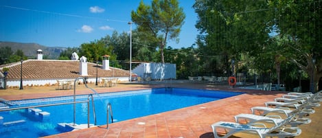 A swimming pool with white lounge chairs, a tiled deck, and a view of a building with a tiled roof.