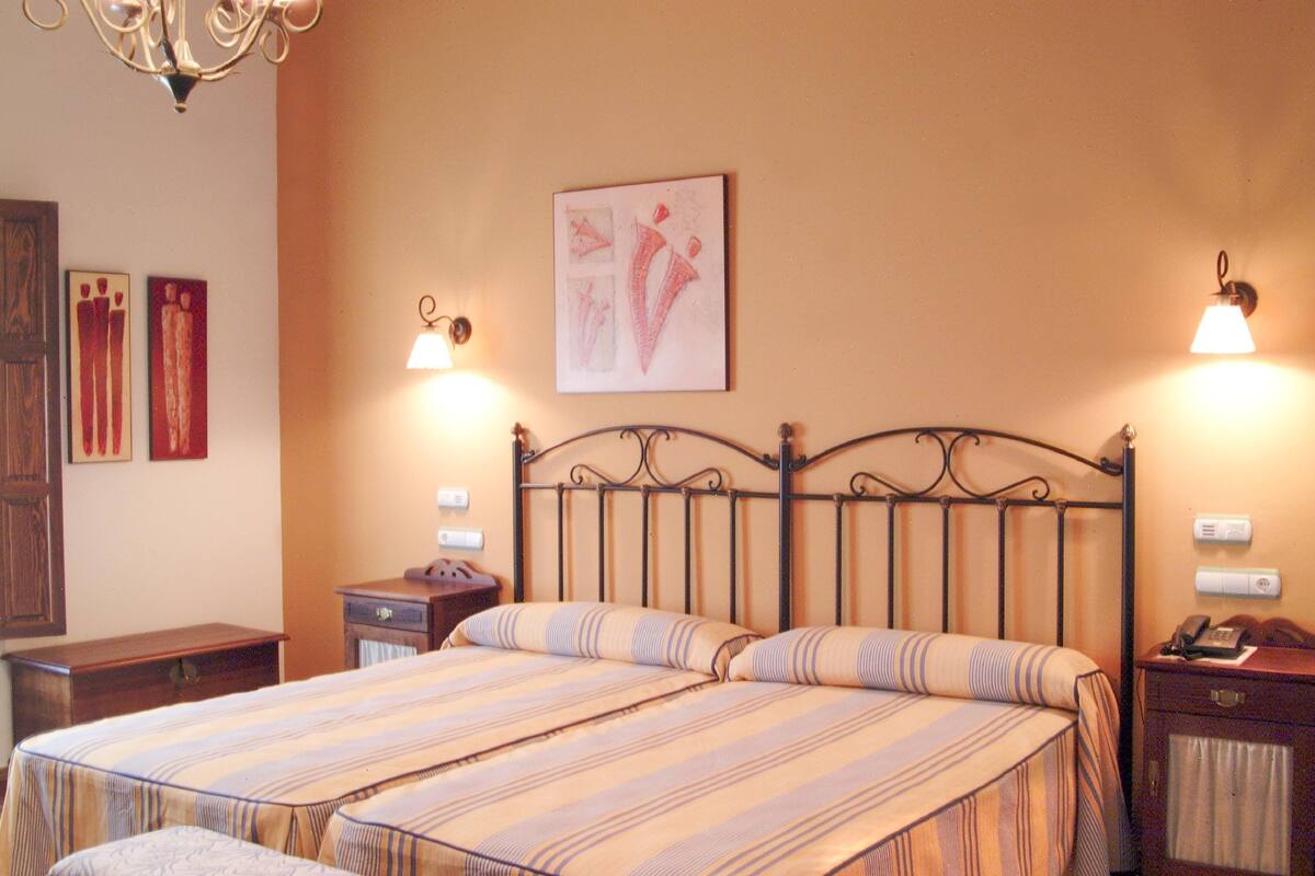 A hotel room with a large bed, two bedside tables, a wall-mounted artwork, and a chandelier.