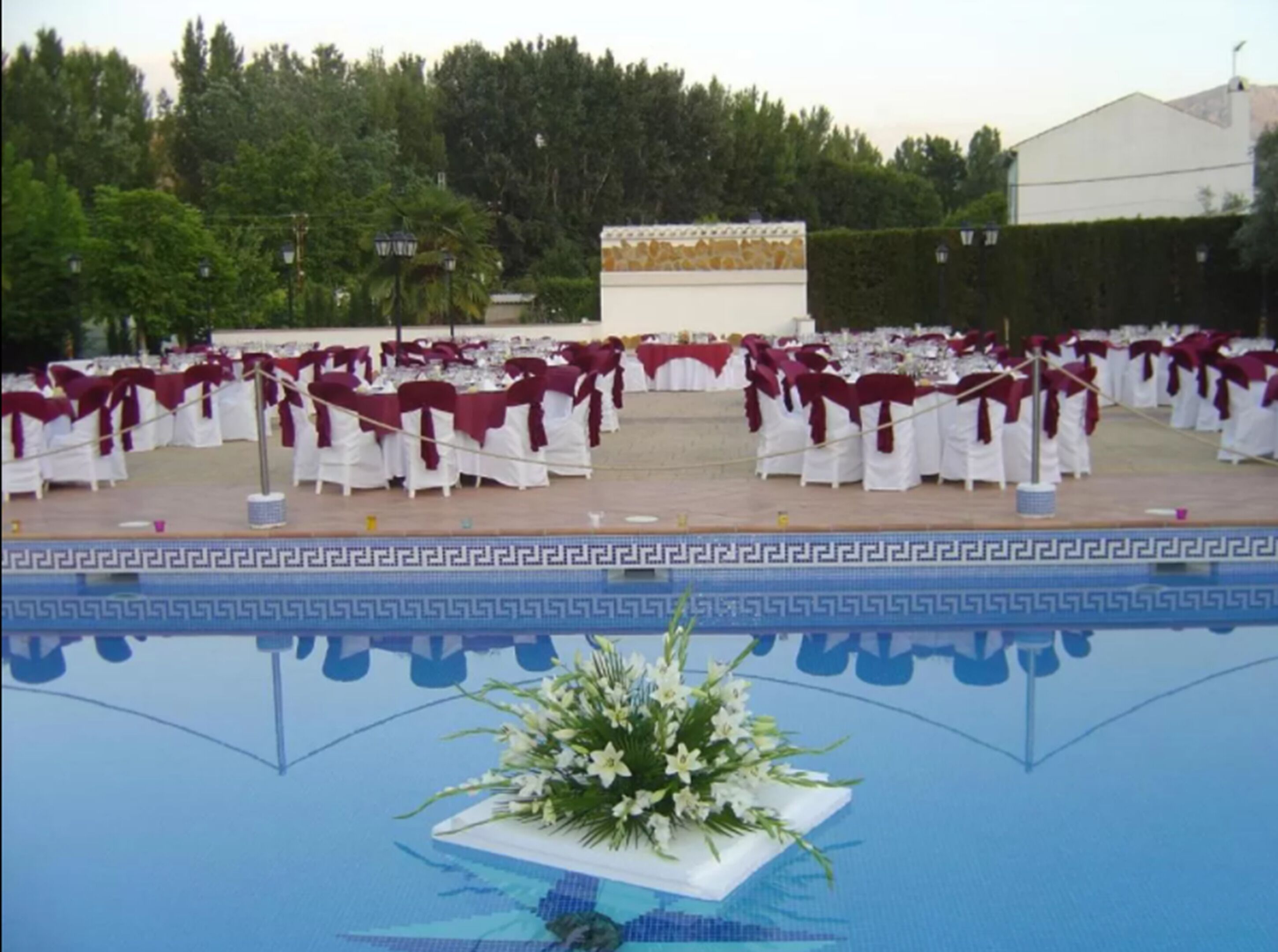 Une salle de banquet avec des rangées de tables et de chaises, une piscine décorative au premier plan et un bâtiment en arrière-plan.