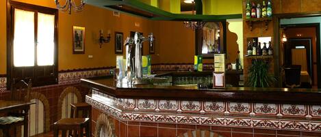 Zona de bar con salpicadero de azulejos, taburetes y una variedad de botellas en estanterías.