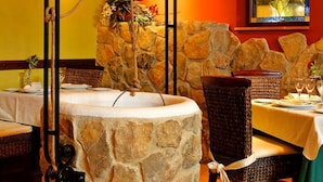 Een stenen fontein als middelpunt in een restaurant, met rieten stoelen en tafels.
