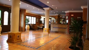 Een hotellobby met een betegelde vloer, grote zuilen, een receptiebalie en zithoeken.